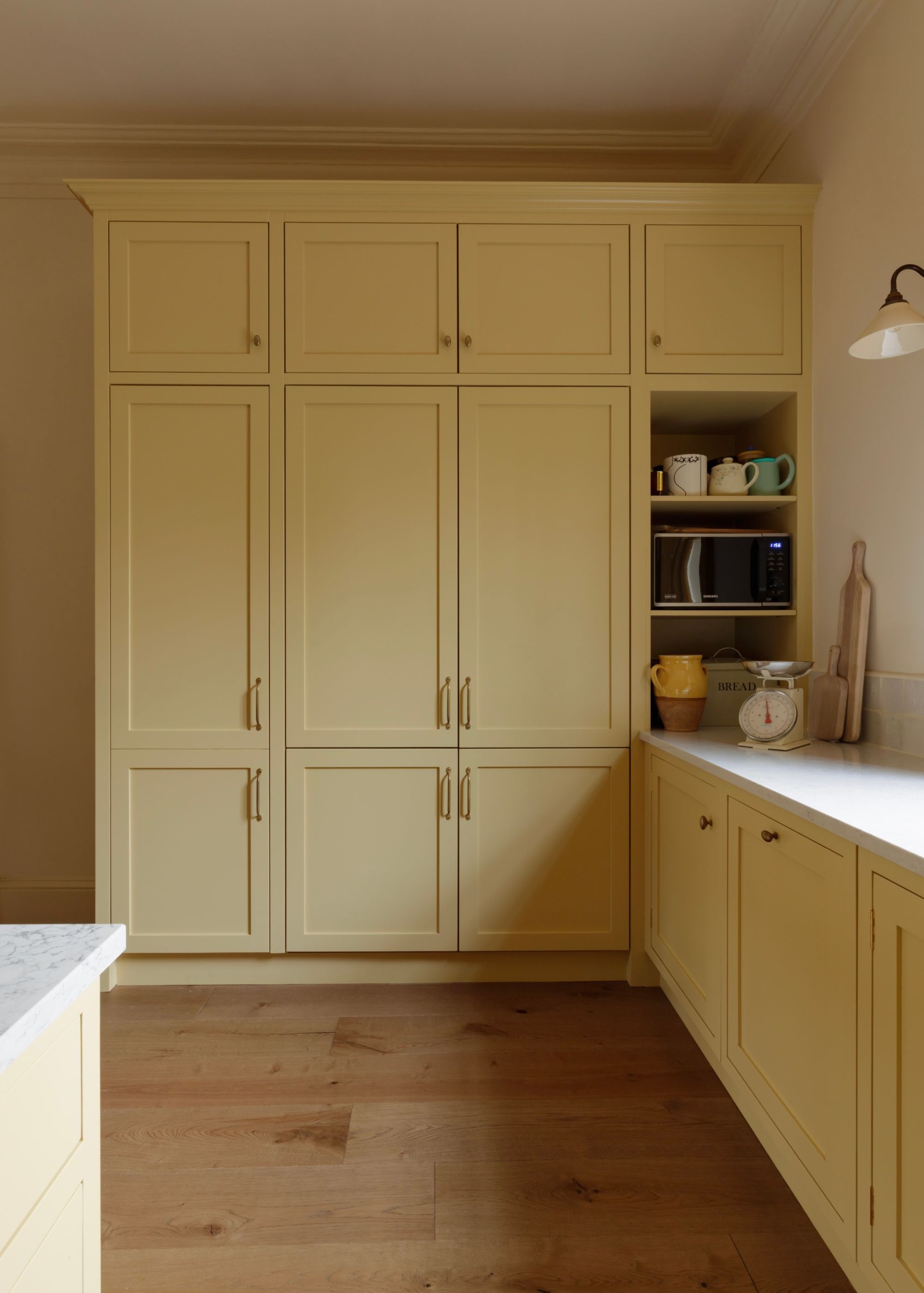 A modern kitchen with butter yellow full-height joinery, wood flooring, off-white walls, and white countertops.