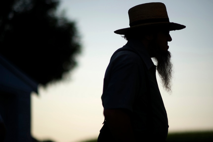 The silhouette of an Amish man with a long, pointed beard extending from his chin, wearing a round-brim hat at dusk.