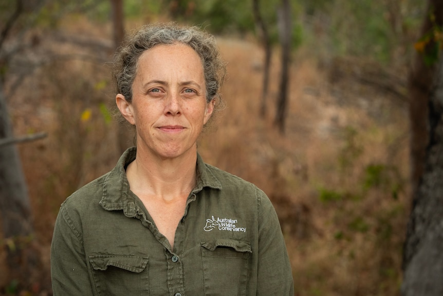 A woman in a green shirt stands in front of bushland.