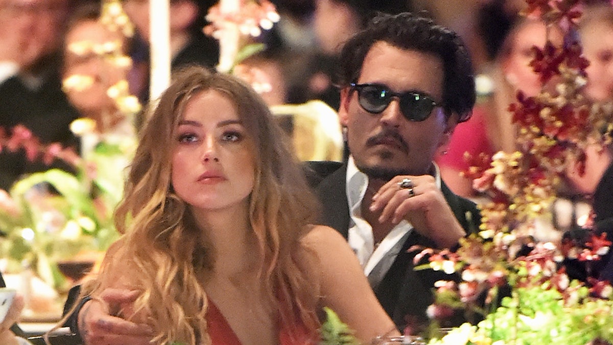 Amber Heard and Johnny Depp sitting together as they look serious.