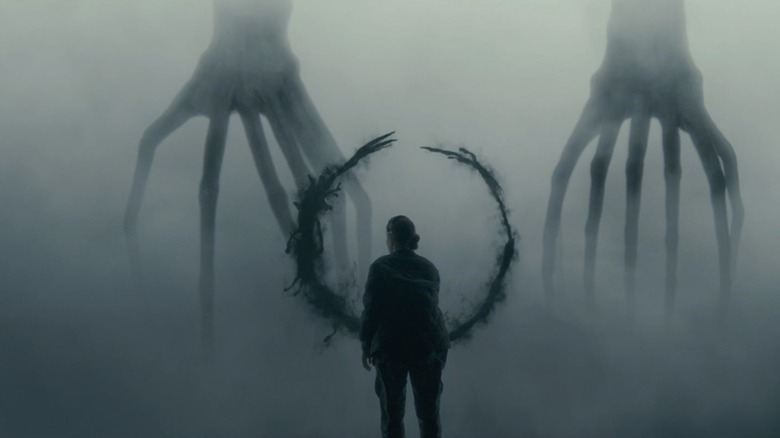 Amy Adams as Louise Banks in Arrival, standing at the barrier between her and the aliens as they make a smoky black ring on the glass.