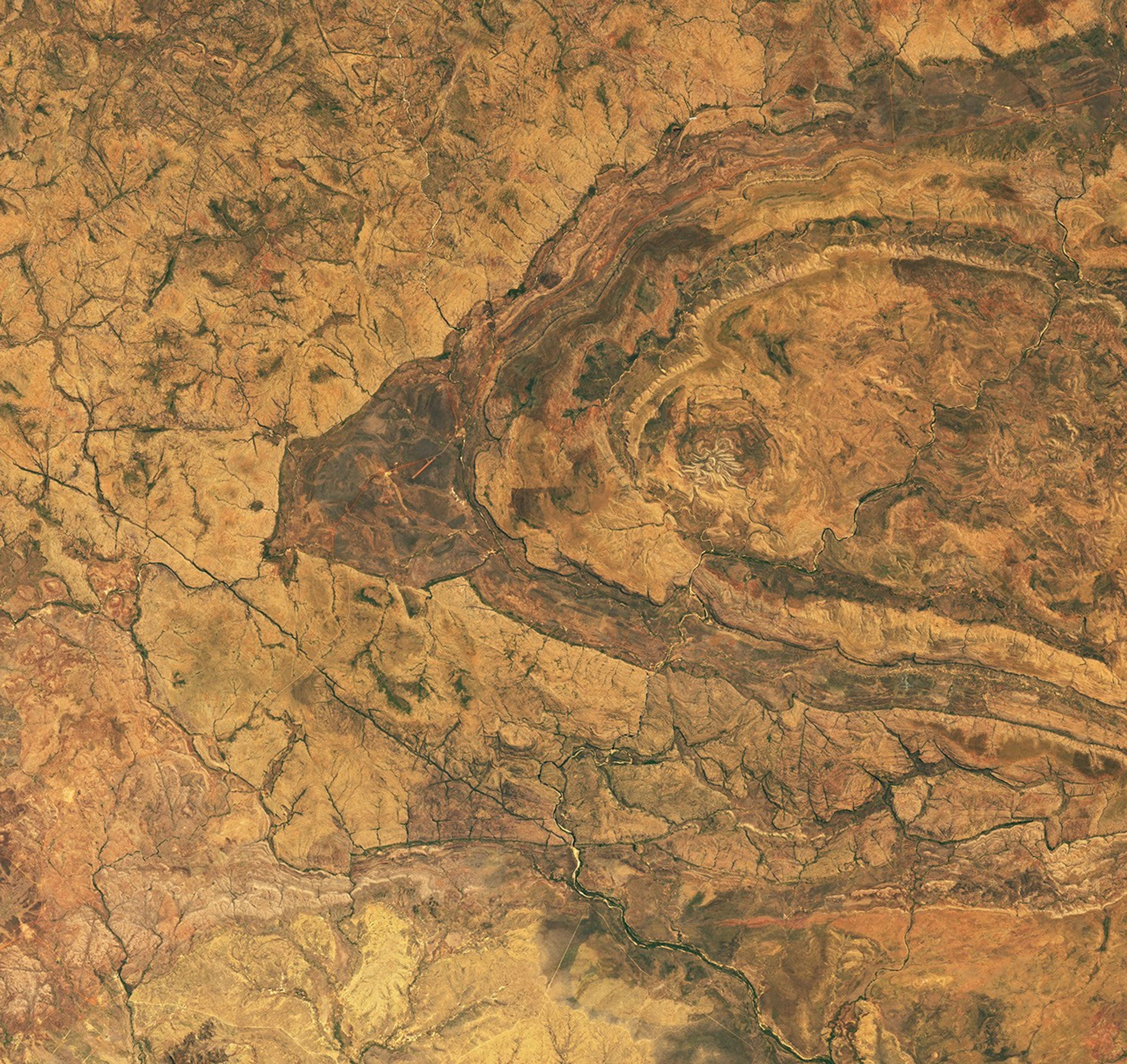 Several short, light-colored rocky ridges radiate out from a central point amid an orange and tan desert landscape.
