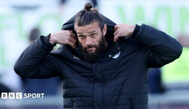 Andy Carroll pulls a hood over his head while walking to the bench during a Dagenham match