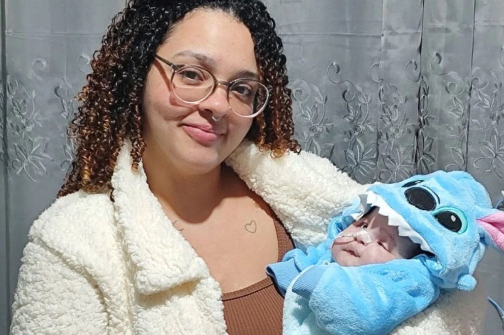 Social worker Leticia Ferreira poses with her daughter, baby Alice Vitória, who is wearing a blue Stitch costume and has a nasal tube.
