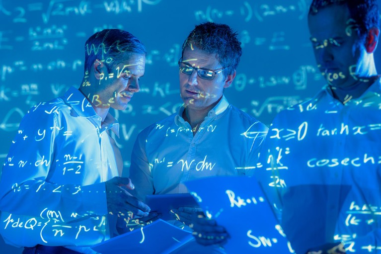 A group of three researchers in conversation are illuminated by projected mathematical formulae.