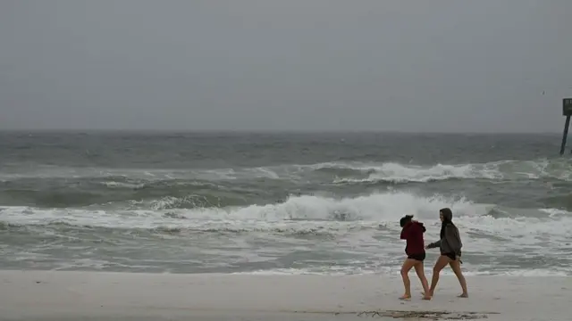 Two women walk on the beach in Navarre, Florida, as Isaias approaches.