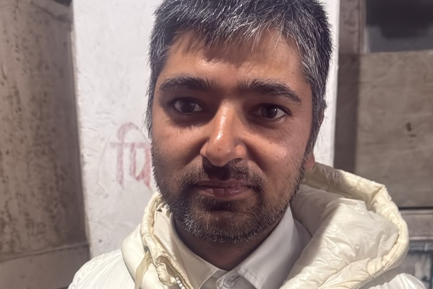 A forlorn man looks to the camera in a white jacket.
