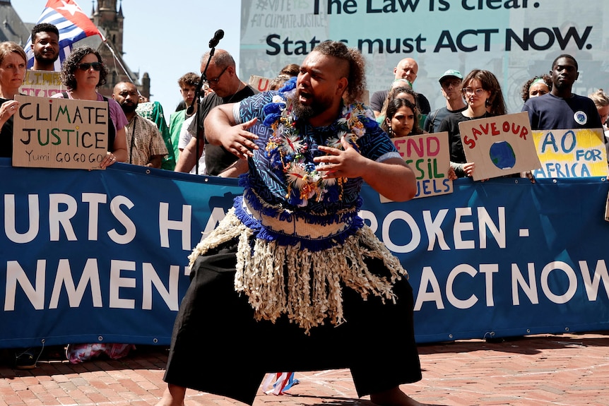 A man in traditional Pacific island dress dances in front of protestors calling for climate action