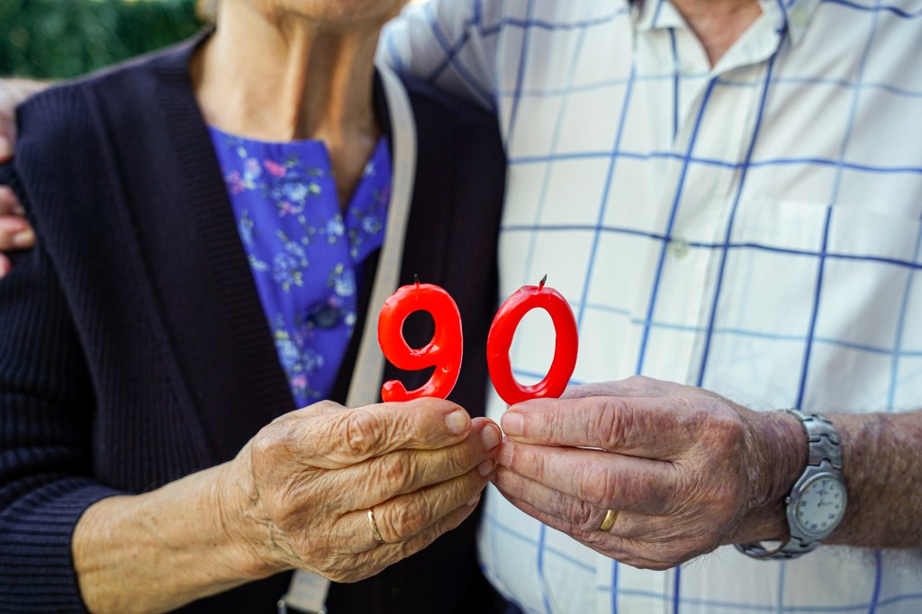 An elderly couple holds red number 90 candles to celebrate their 90th birthday.