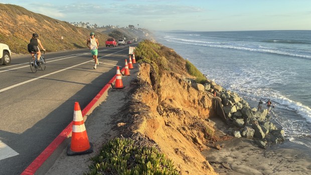 Cars and runners on Carlsbad Boulevard pass an area where Carlsbad has declared an emergency to expedite the extension of a rock revetment.