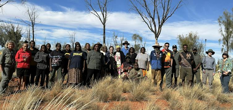 A large group of traditional owners and scientists standing together in a desert landscape.