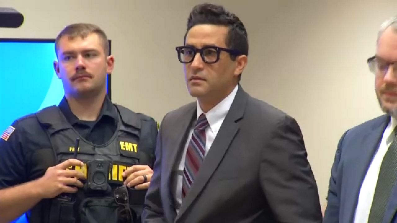 luciano frattolin stands in court between a sheriff's deputy and a lawyer