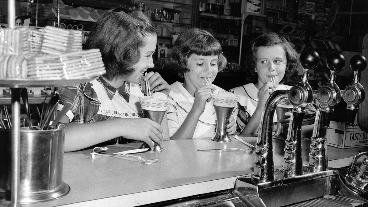 Three girls drink ice cream floats from a counter in 1952.