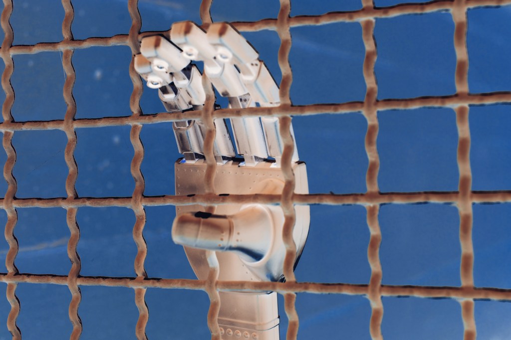Hand of a robot in a jail cell with bars.