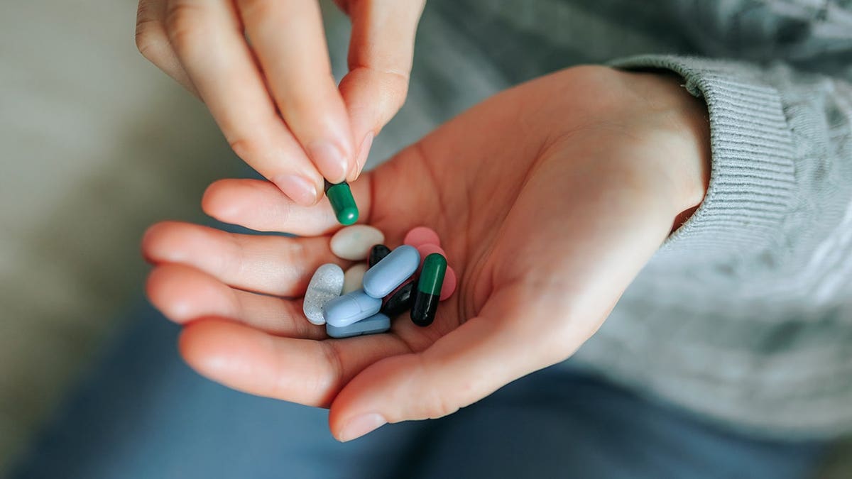 Woman's hand holds a handful of colorful pills in close-up.