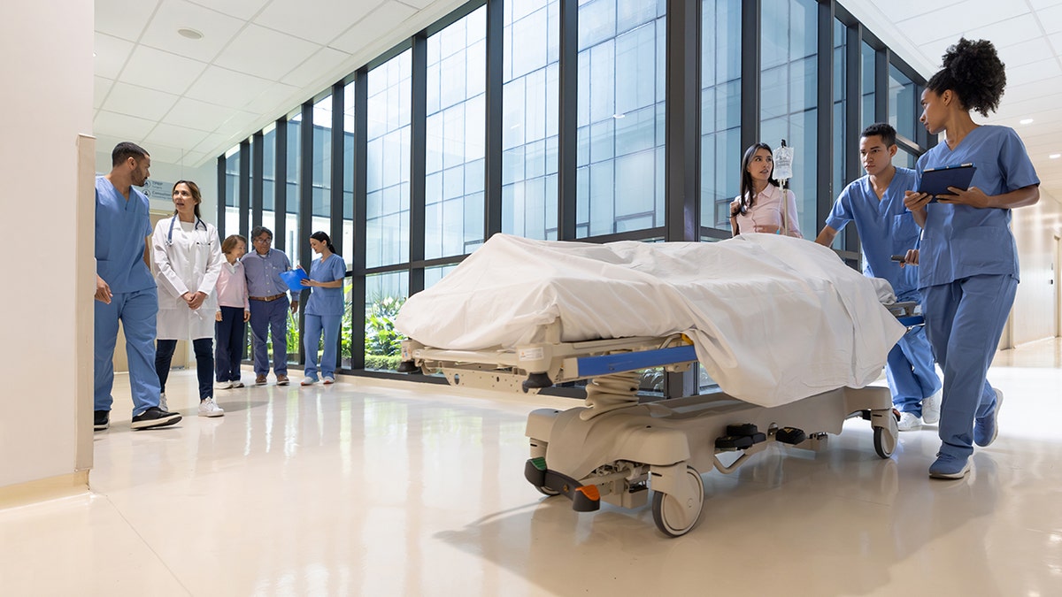 Group of healthcare workers moving a patient in a gurney at the hospital - healthcare and medicine concepts