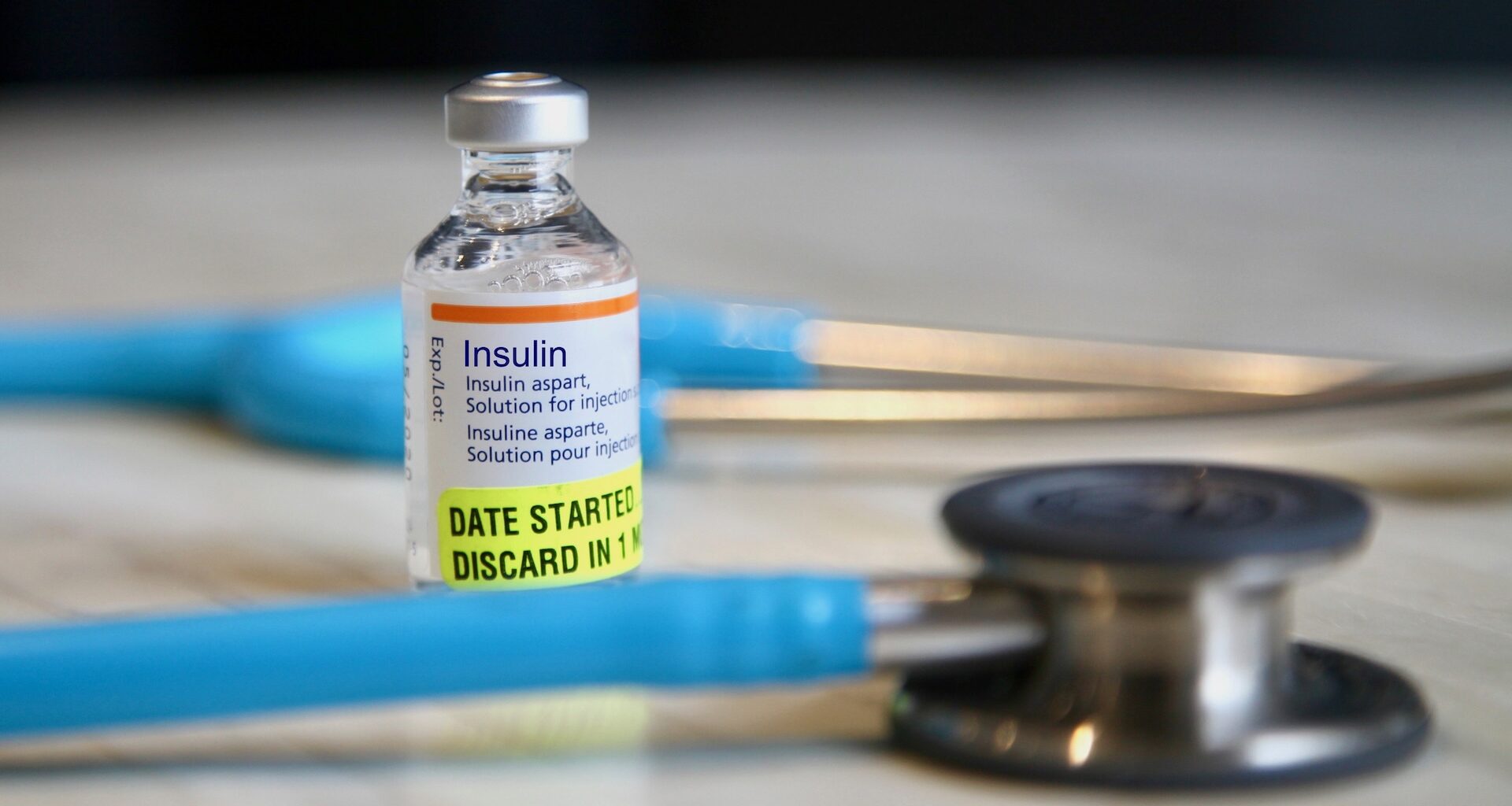 A vial of insulin beside a stethoscope and syringes on a table.