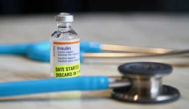 A vial of insulin beside a stethoscope and syringes on a table.