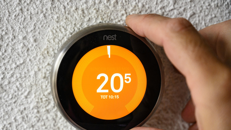 A  hand adjusting a Google Nest thermostat.