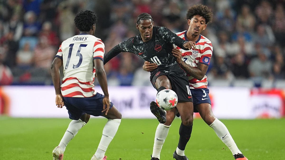 Jonathan David battles for the ball against Brooklyn Raines and Chris Richards during a soccer match.