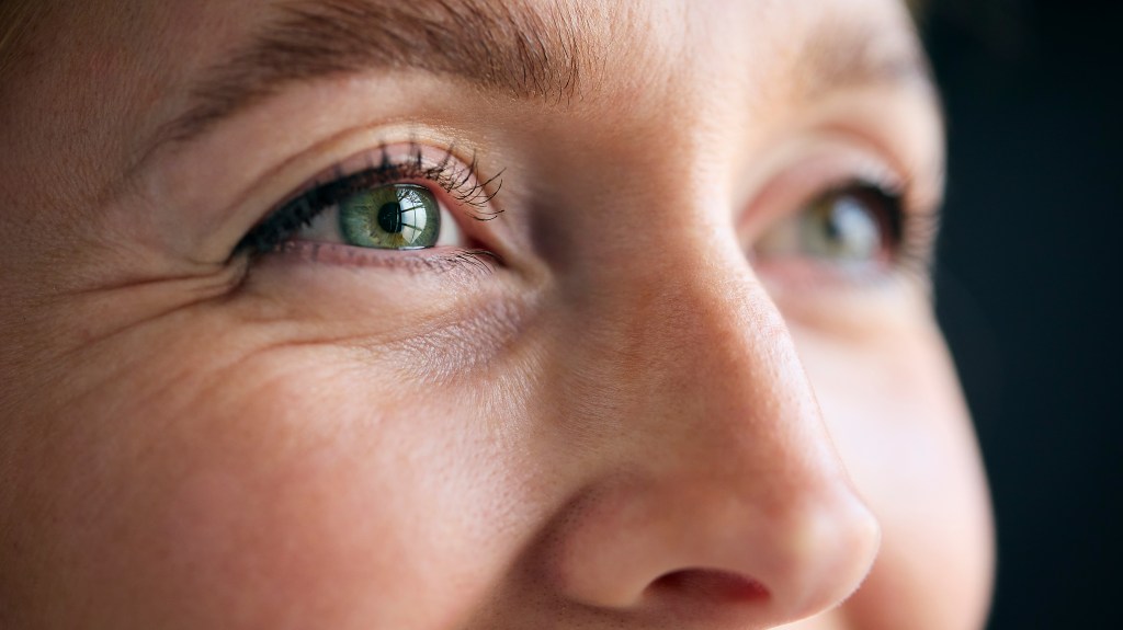 Macro shot of a woman's smiling green eyes, eyelashes, and pupil.