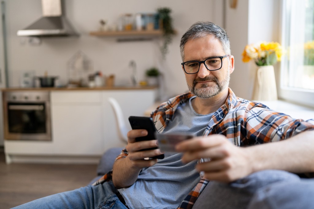 A man types his social security number on a mobile phone from home.