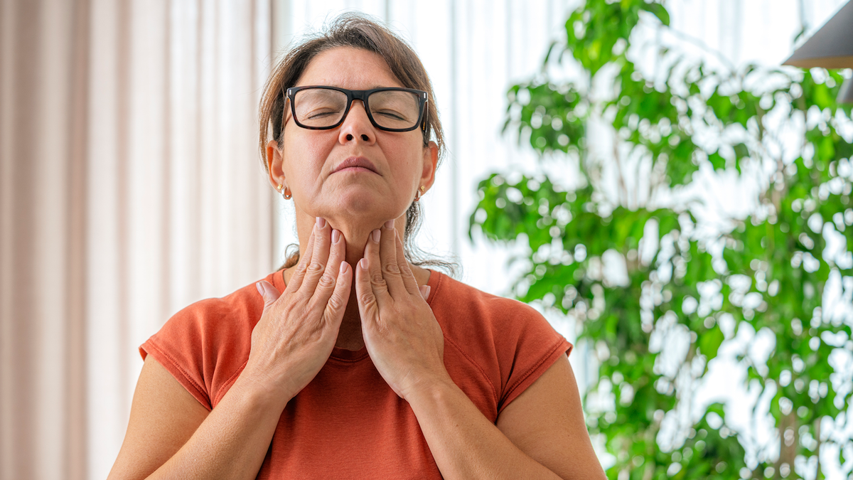 Mature woman touching her sore throat with both hands.