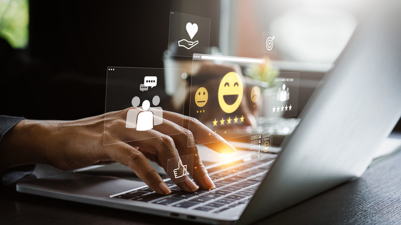 Holographic image of different emojis and star ratings above a laptop.
