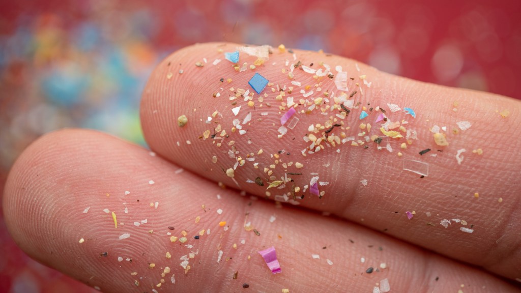 Microplastic particles rest on a human finger for scale, illustrating water pollution and environmental impact.