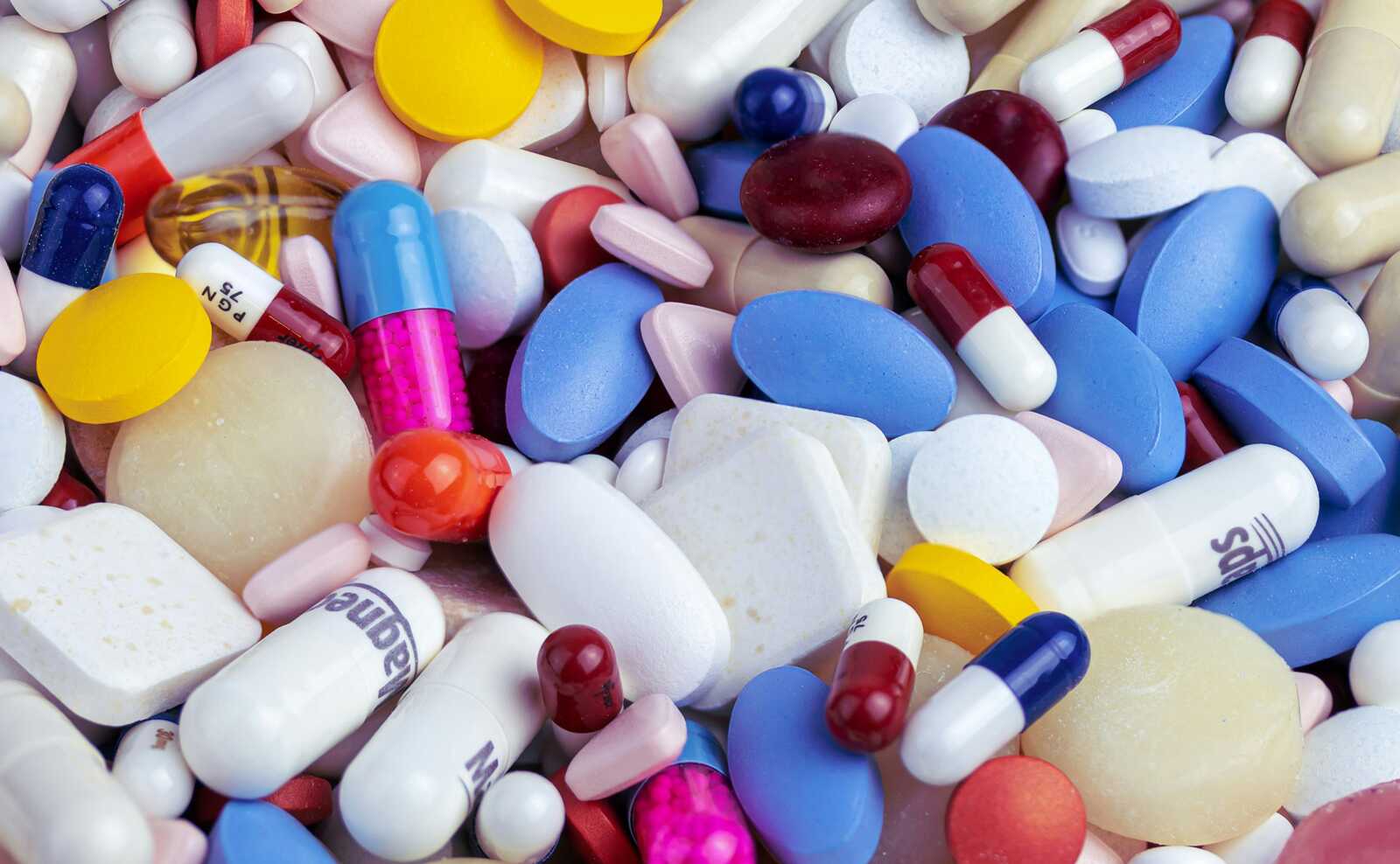 Assorted pills, capsules, and tablets in various colors and shapes scattered together.