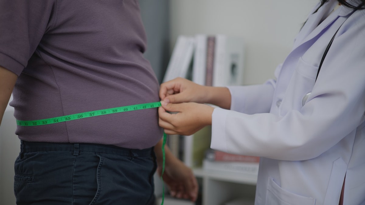 Female Nutritionist measuring waist of overweight man in weight loss clinic during giving consultation to patient with healthy and diet weight loss, Right nutrition and diet concept