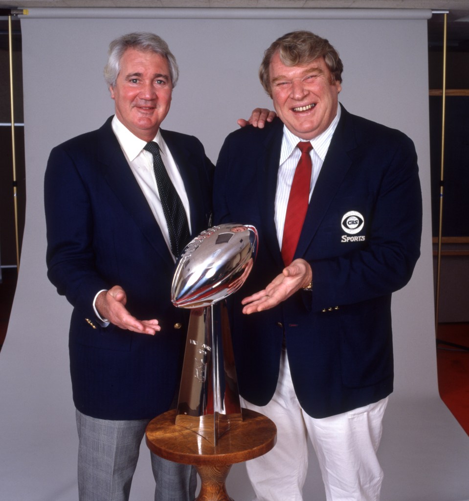 Pat Summerall and John Madden posing with the Super Bowl XVIII trophy.