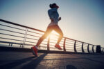 A woman running outdoors along a waterfront path in sunlight.