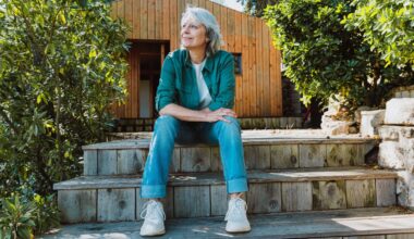 Senior woman relaxing on rustic wooden stairs, looking thoughtfully into the distance, embracing a peaceful outdoors retirement lifestyle at her simple wooden cabin surrounded by nature