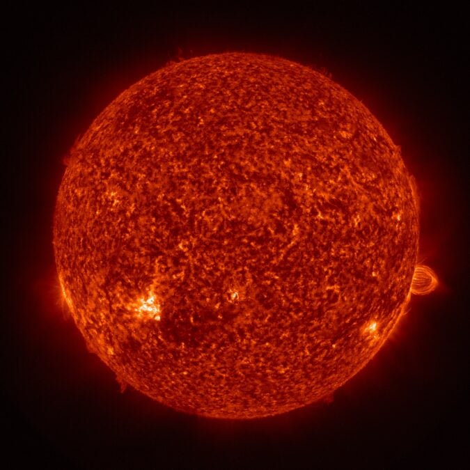 Bright orange loops of plasma rise above the Sun's edge against a black background in a colorized ultraviolet image.