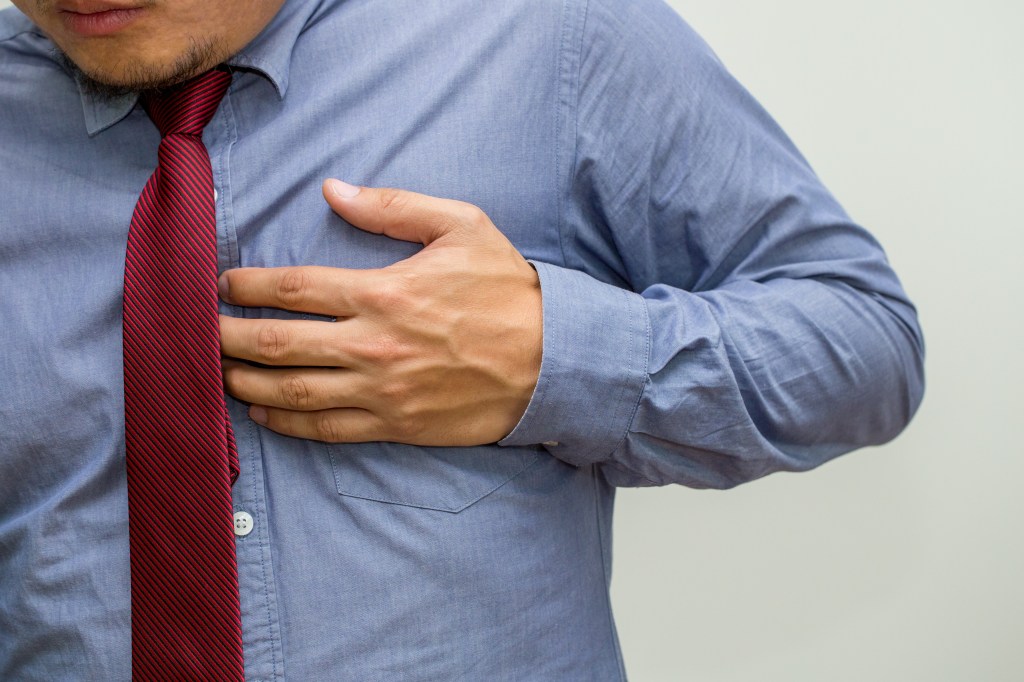 A man in a blue shirt and red tie holding his chest in pain, indicating a symptom of heart disease.