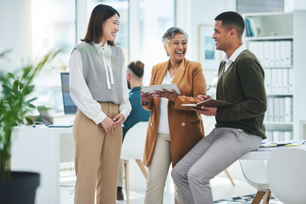 A diverse group of business professionals laughing and talking in an office.