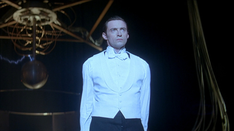 Hugh Jackman as Lord Caldlow/Robert Angier in The Prestige, standing under the spotlight in a white shirt and vest.