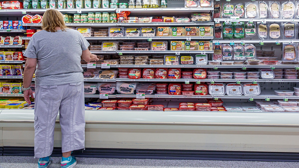 Woman seen from behind shopping for packaged lunch meats.