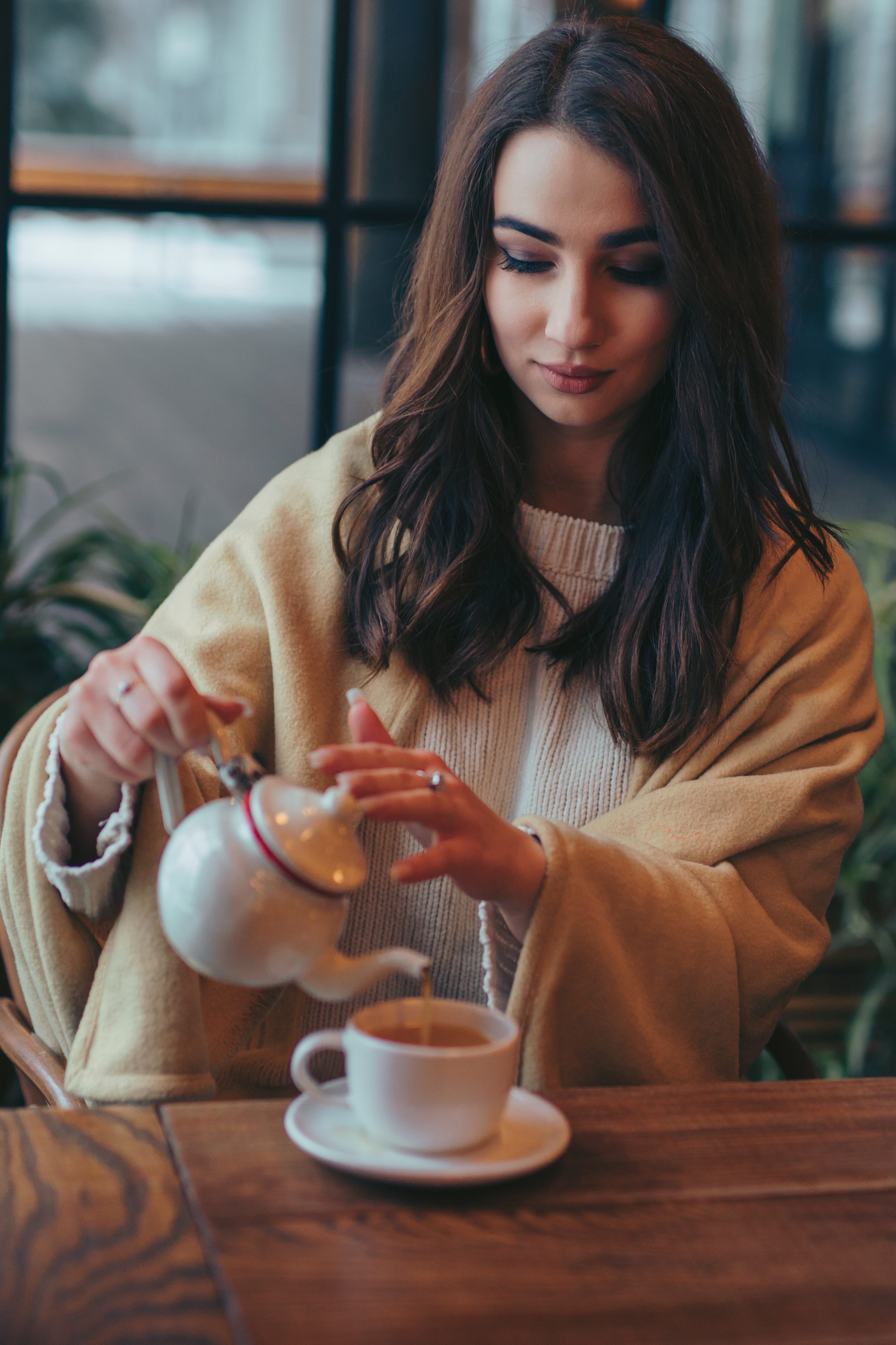 A woman pours tea from a white teapot into a cup at a cafe.