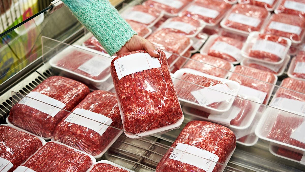 A woman chooses a package of ground beef from a grocery store cooler.