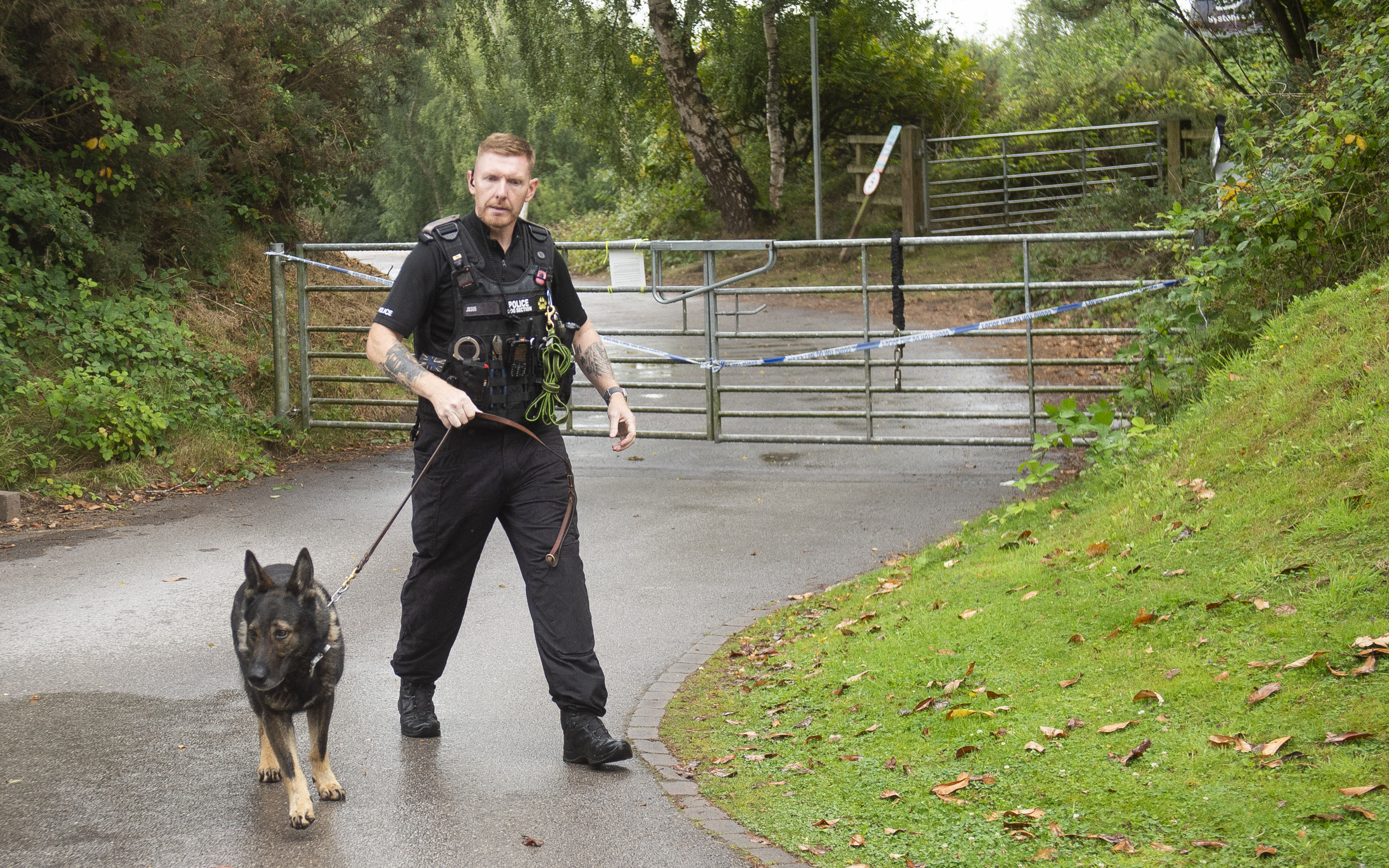 Police officer with dog at a gated entrance.