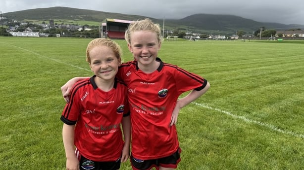 Fiadh Ní Charthaigh and Méadhbh Ní Chorcoráin stand on a gealic pitch.