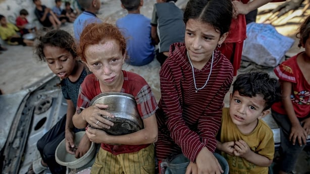 Four young children are seen holding pots as they wait to receive hot food distributed by a charity organisation in Gaza City