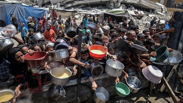 A crowd of people holding pots and plastic basins plead for food at a charity kitchen in Gaza City