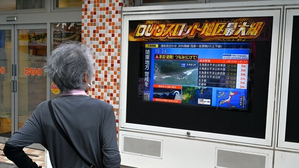a woman looking at a tv screen regarding a Japanese tsunami warning