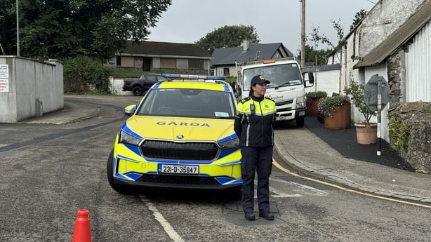 A female garda stands in front of a garda car with houses in the background