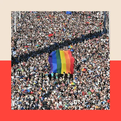 Attila Kisbenedek via Getty A mass of people at Budapest pride, with a large LGBT flag being carried by the crowd