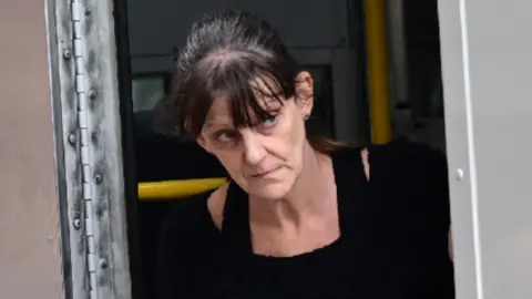 Wales News Service A woman with dark hair walking out of a police van. She had a black jumper dress on