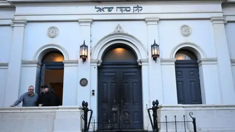JAMES ROSS/EPA/Shutterstock Fire marks on the blue door of the East Melbourne Hebrew Congregation in Melbourne, with two men to the left in front of an open window